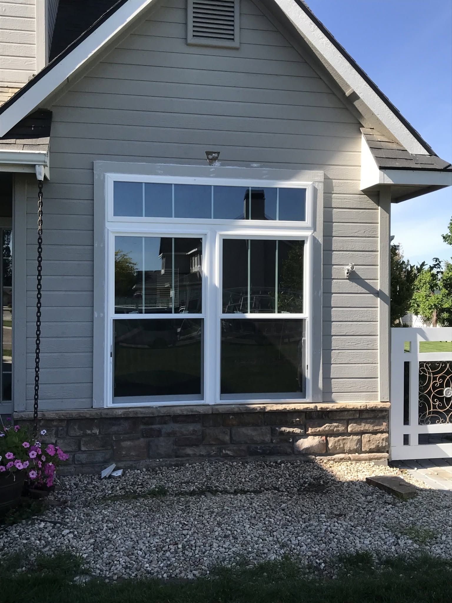 House exterior with a large white-framed window, gray siding, and gravel landscaping.