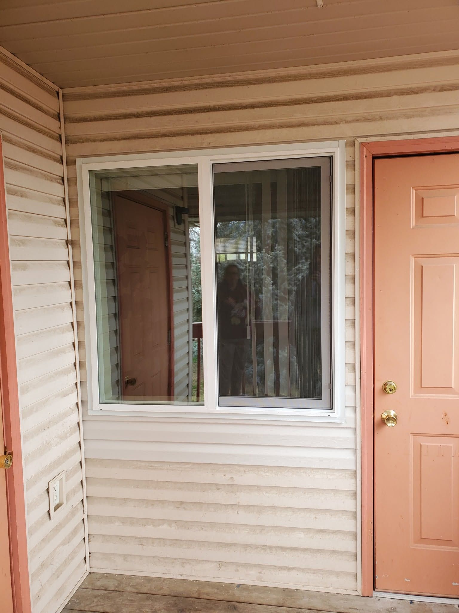 Front porch with a white-framed window beside a peach-colored door and beige siding