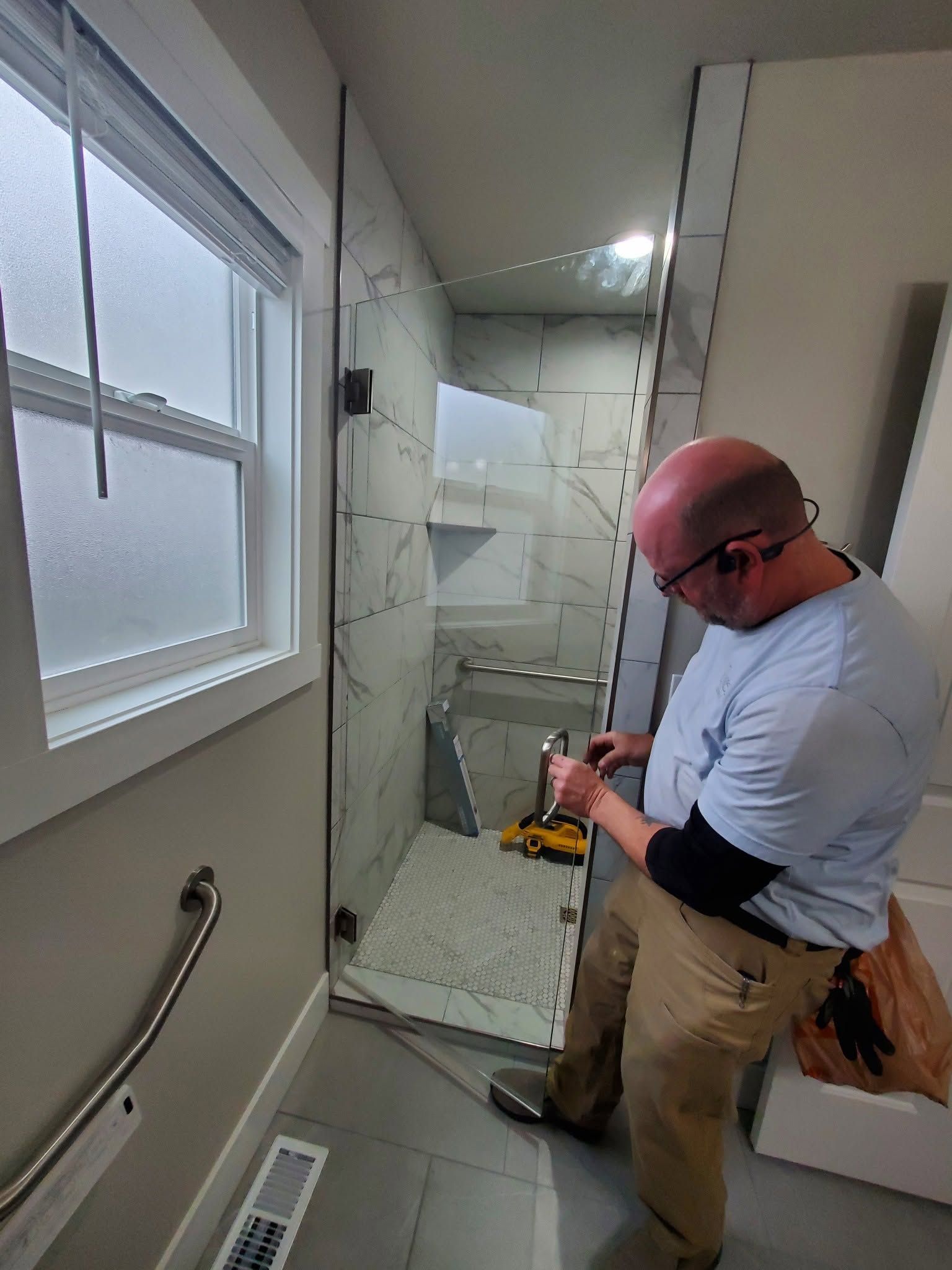 Worker in a bathroom under renovation, standing beside a shower stall with tools and exposed wall panels.