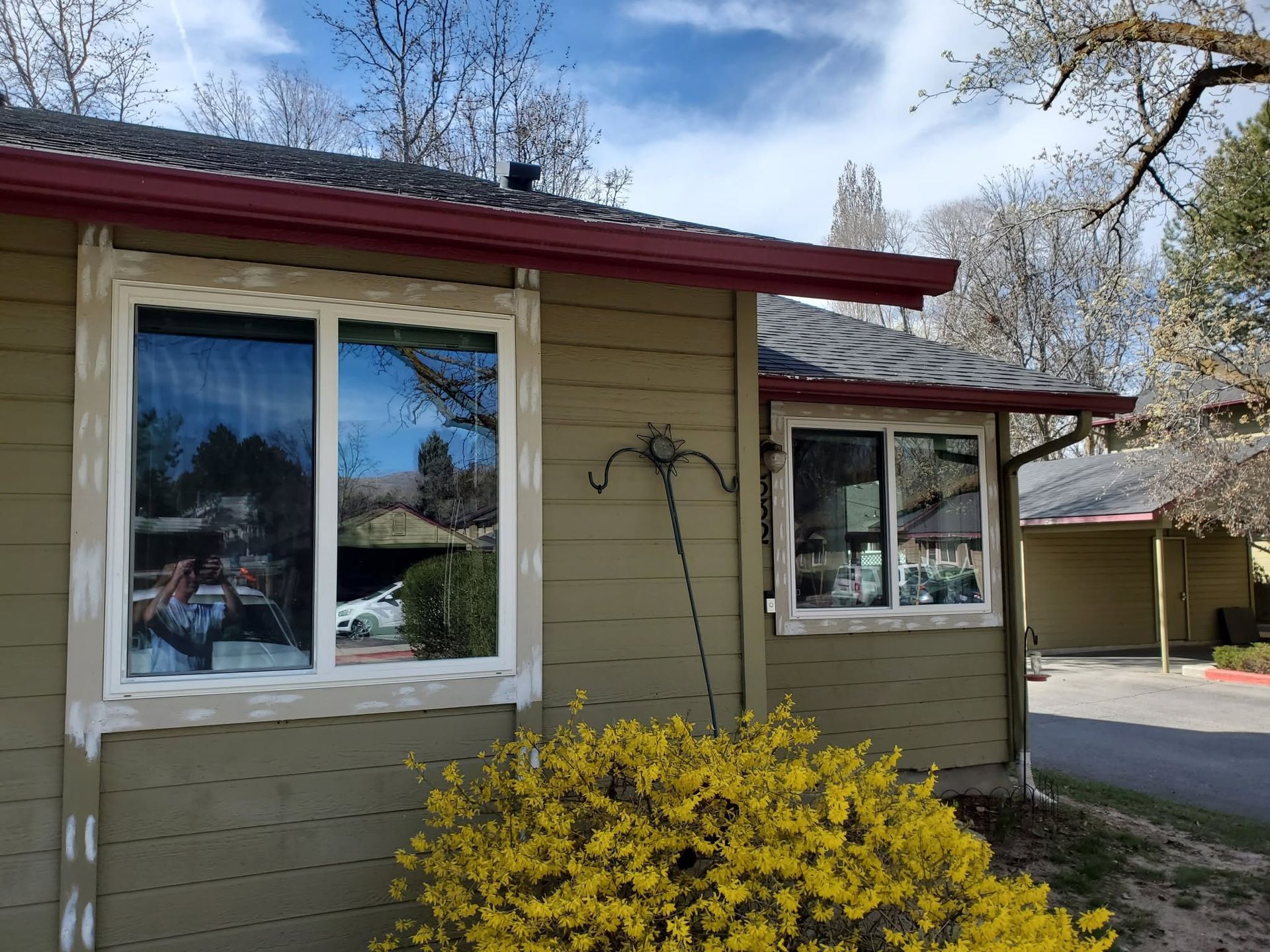 Small beige house with white-trimmed windows, red roof, and yellow bush in front under a blue sky.