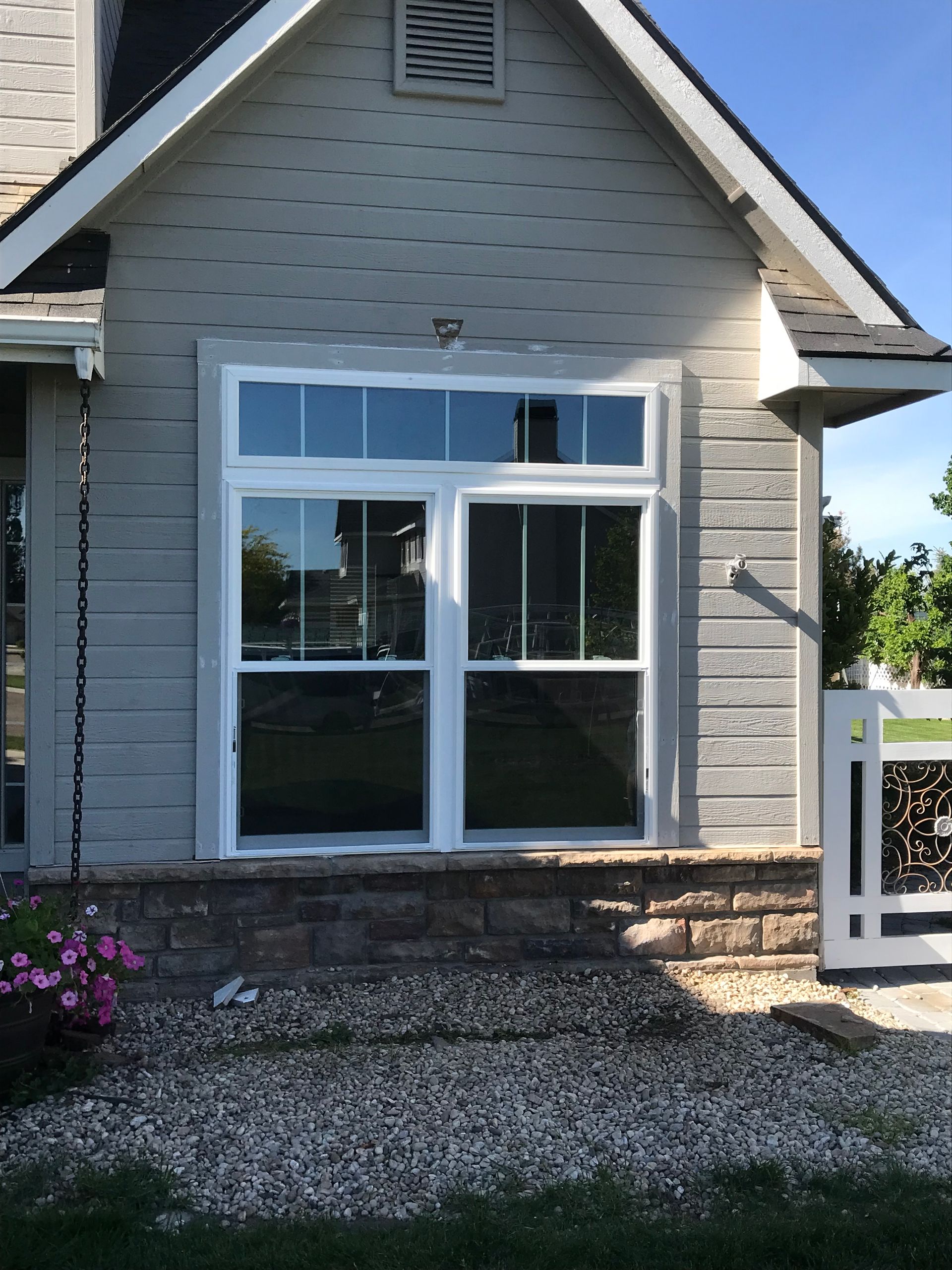 Front of a gray house with a large white-framed window and gravel walkway