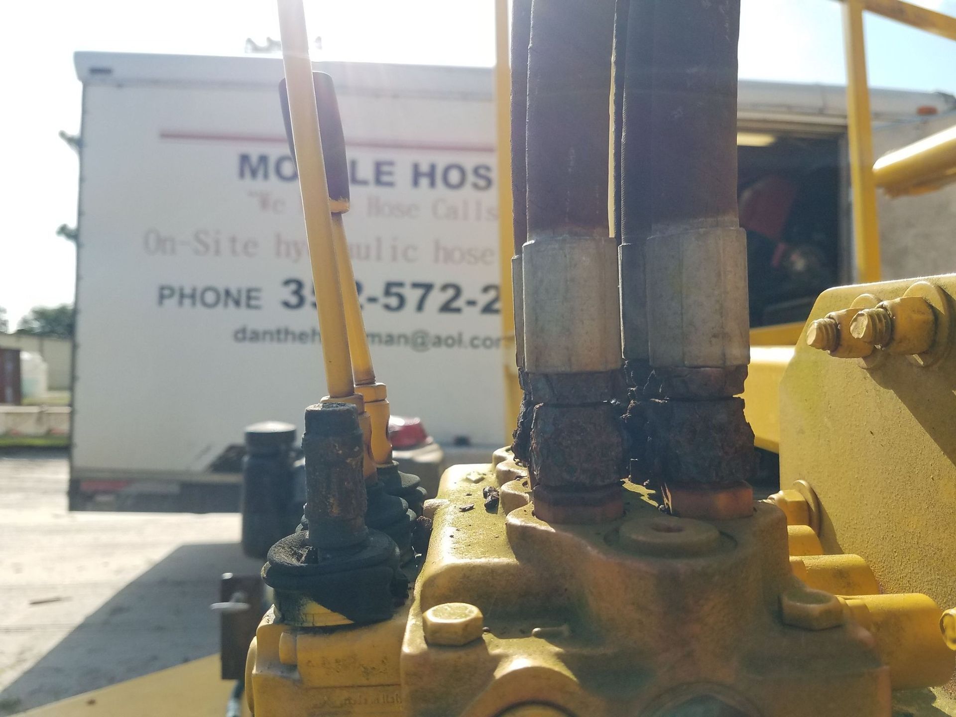 Yellow construction equipment with hydraulic hoses, in front of a mobile hose repair truck.