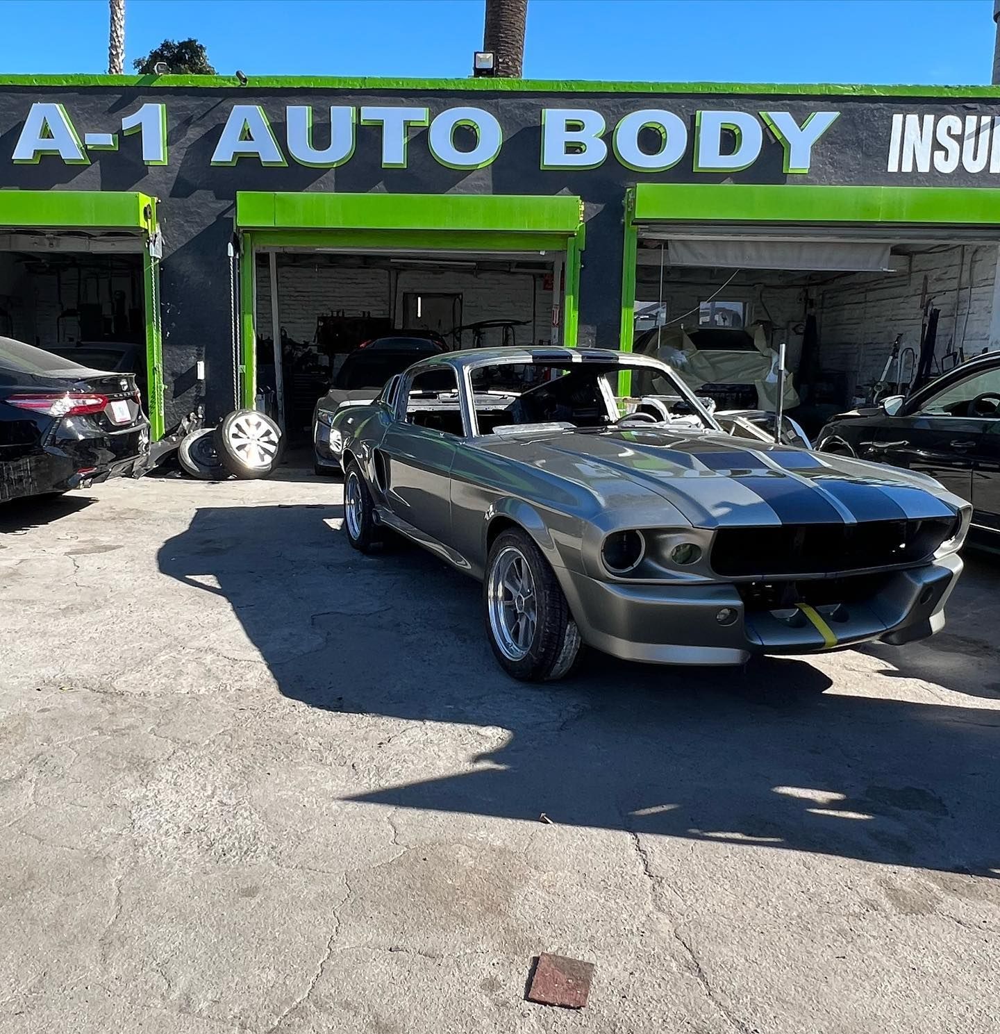 A gray mustang is parked in front of a a-1 auto body shop.