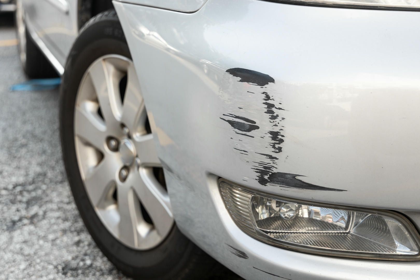 A white car with a damaged bumper is parked on the side of the road.