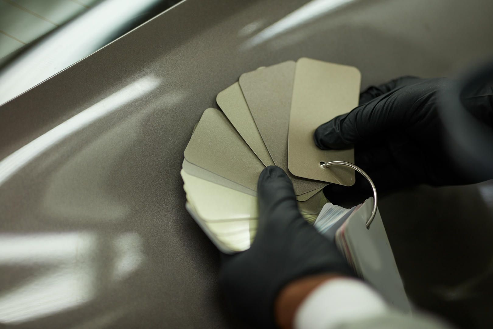 A person wearing black gloves is holding a fan of paint samples.