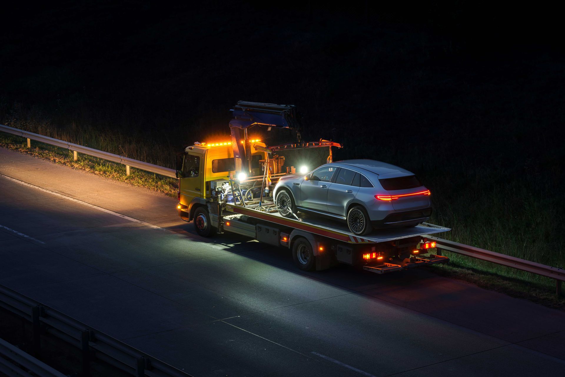 A tow truck is towing a car on a highway at night.