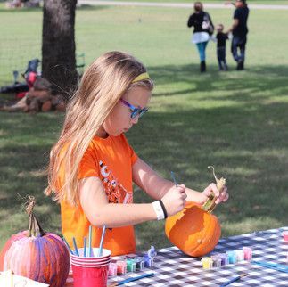 A little girl is sitting at a table painting pumpkins.