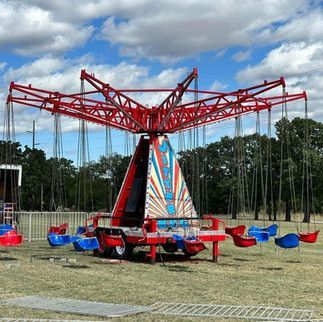 A red and blue swing ride is sitting in the middle of a field.