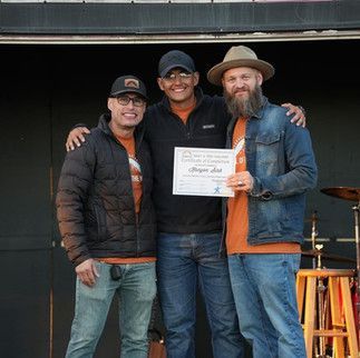 Three men are posing for a picture and one of them is holding a certificate.