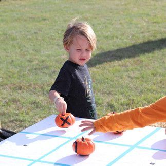 Two children are playing a game of tic tac toe with pumpkins
