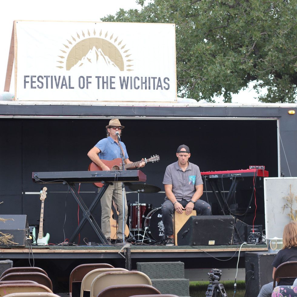 A man playing a guitar and another man playing a keyboard at the festival of the wichitas