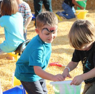 A boy with his face painted has a bucket in front of him.