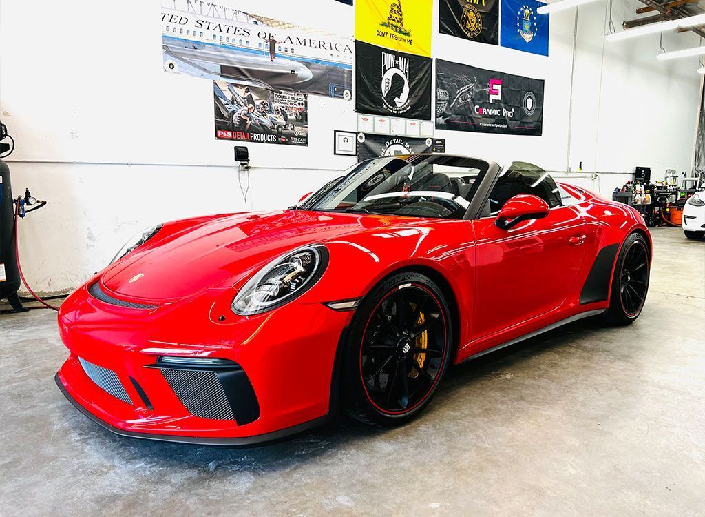 Red sports car in a showroom, glossy paint with black wheels and soft top down.