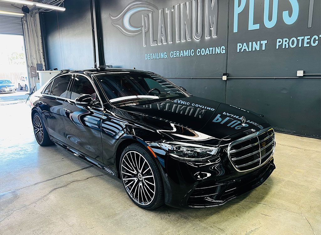 Black sedan in a car detailing shop beside a “Titanium Plus Paint Protect” wall sign
