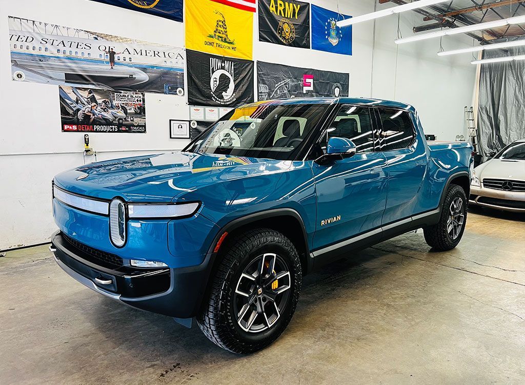Blue Rivian pickup truck displayed indoors in a showroom, front three-quarter view