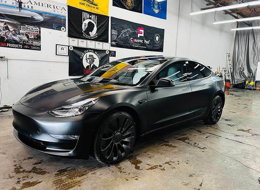 Black sedan in an indoor garage with wall posters and wet floor