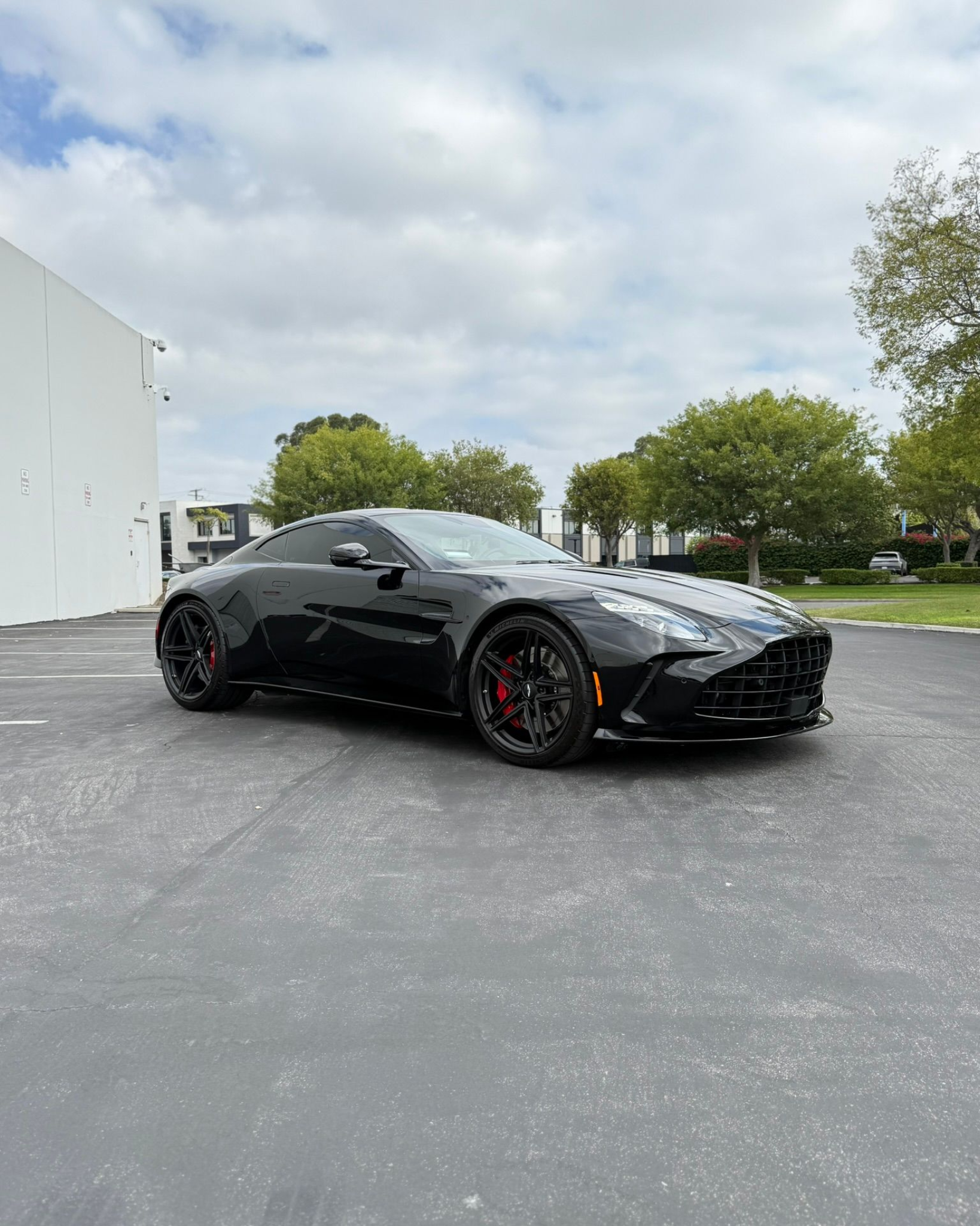 Black sports car parked on asphalt outside a white building on a cloudy day