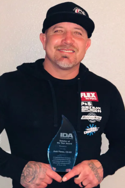 Man holding a clear award plaque, wearing a black cap and hoodie, smiling against a plain background