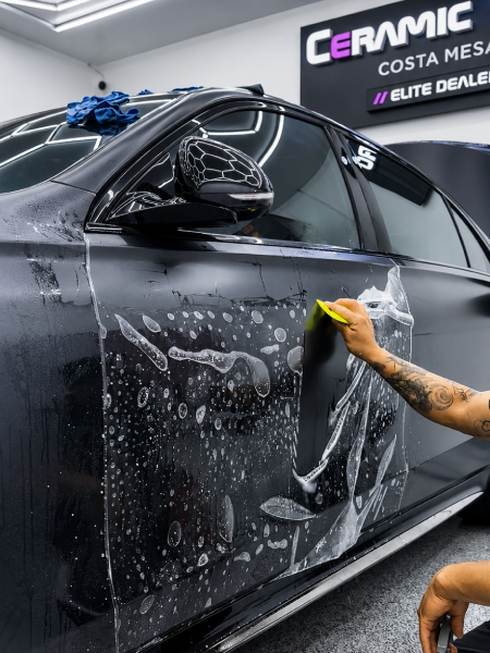 Person washing a black car’s side window and door with soap in a detailing shop