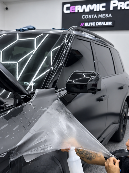 Black SUV being wrapped with protective film in a car detailing shop