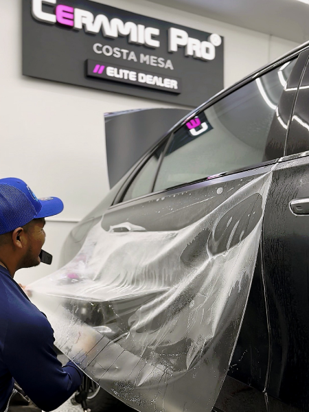 Technician applying clear protective film to a black car at Ceramic Pro Costa Mesa