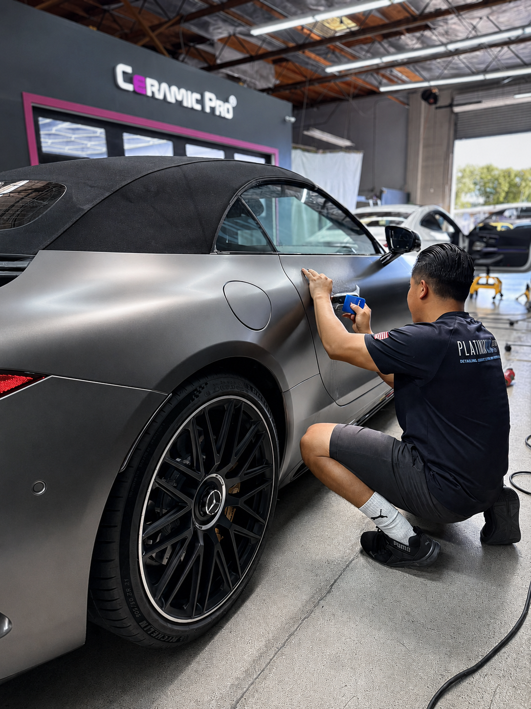 Worker polishing a matte gray car in an auto detailing shop with a buffer tool