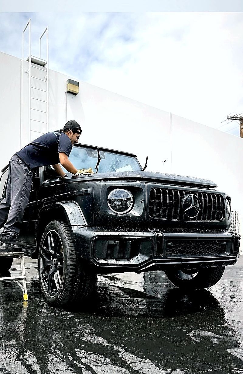 Person washing a black SUV outdoors with a hose on a wet driveway
