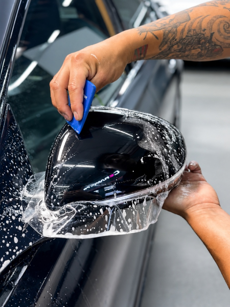 Hands washing a black car side mirror with soap and water