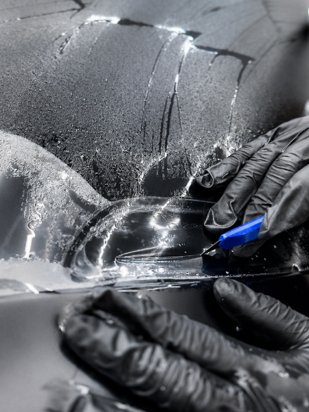 Gloved hands applying clear film to a car headlight with a blue squeegee