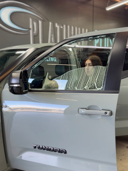 Silver Jeep with open driver door at a dealership, showing a person seated inside behind cracked glass.