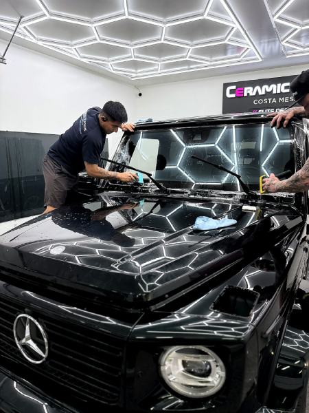 Detailing worker polishing a black Mercedes in a bright car wrap shop with geometric ceiling lights