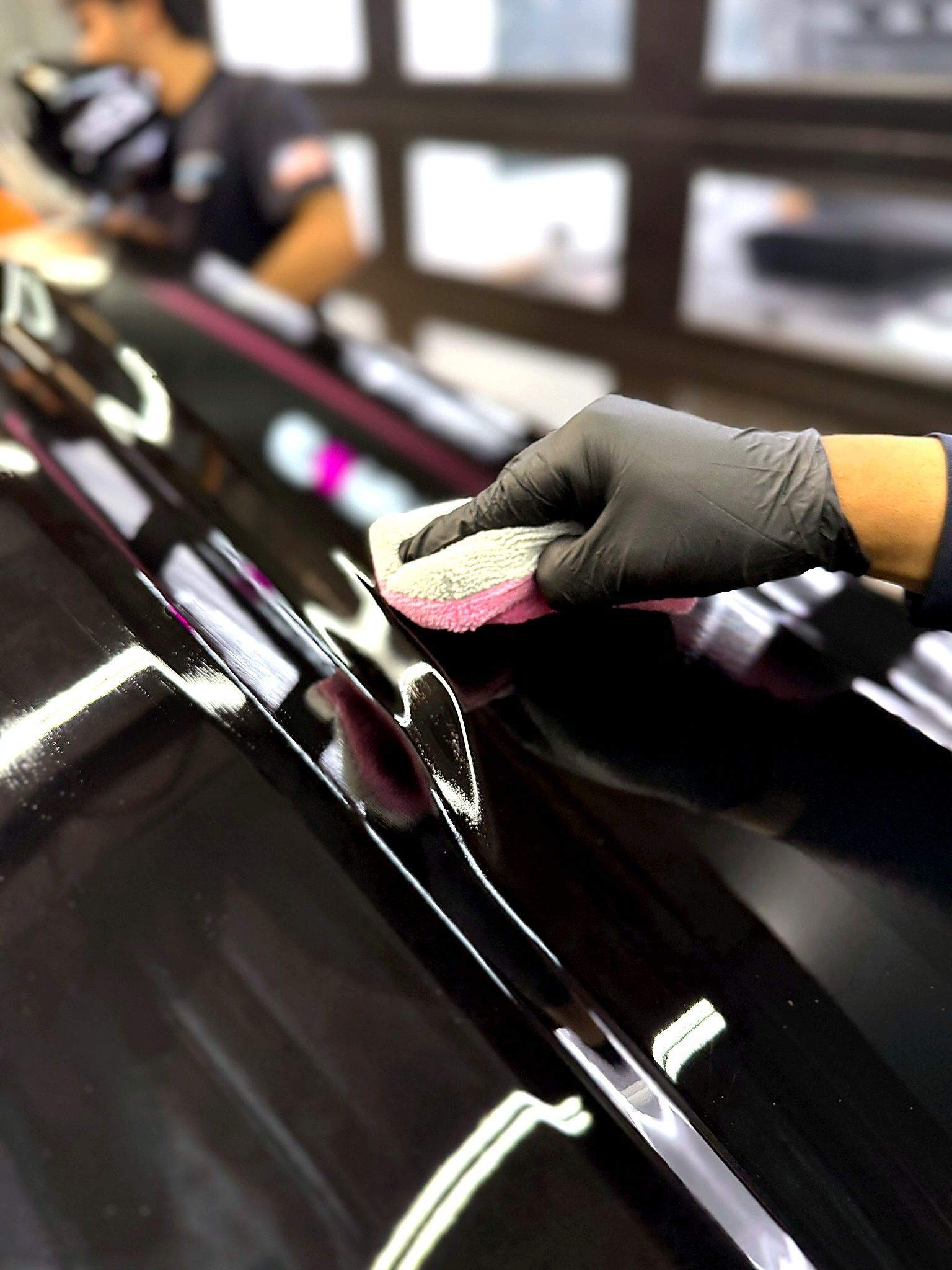 Gloved hand polishing a glossy black car surface with a cloth.