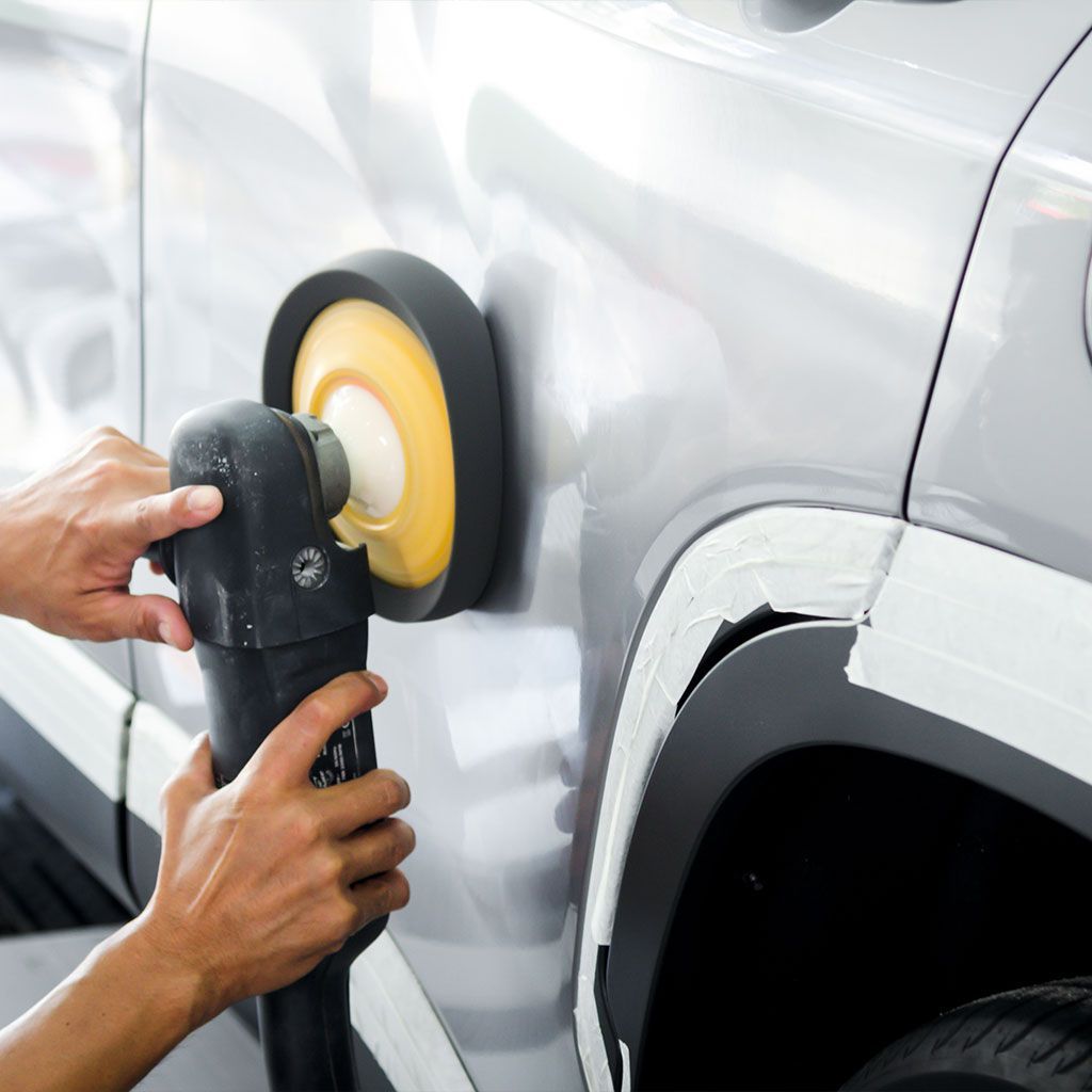 Person polishing a silver car door with a power buffer near the wheel well