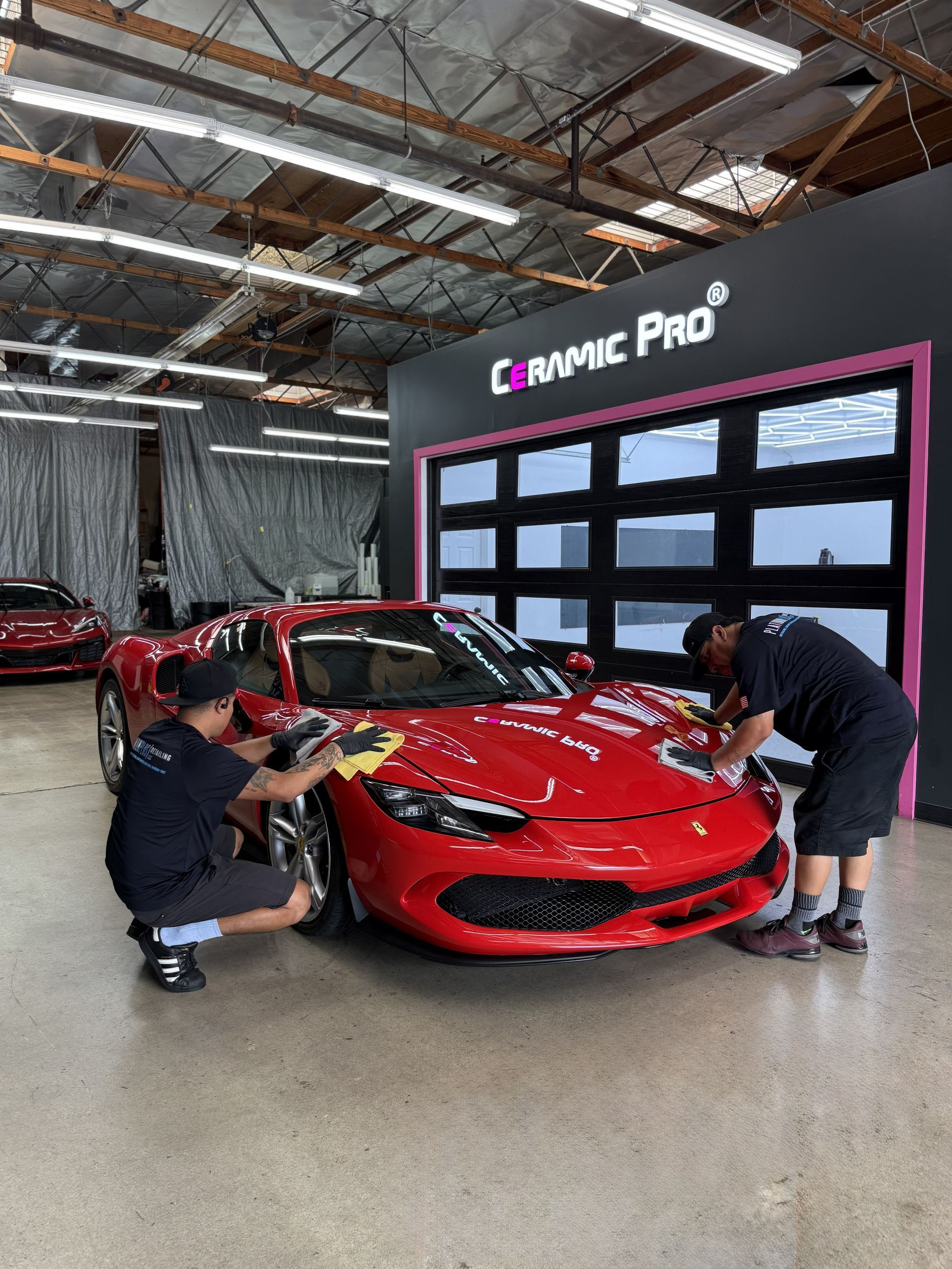 Two technicians inspect a red sports car in a garage with a black display wall.