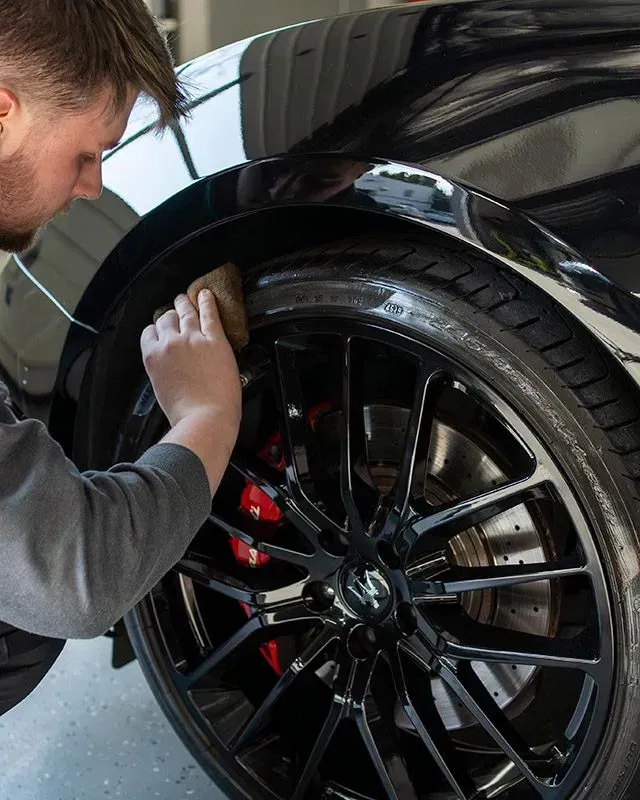 Person cleaning a black car wheel with a cloth in a garage
