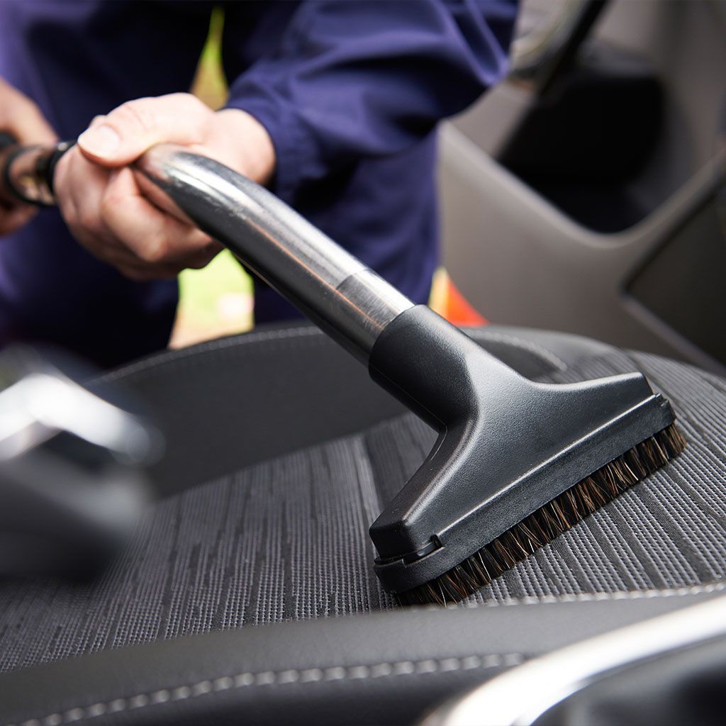 Hand using a vacuum brush to clean a car seat upholstery