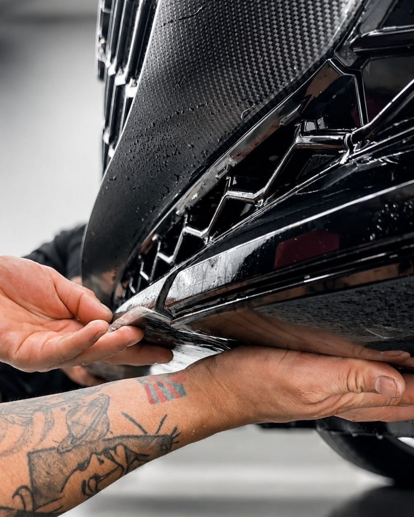 Hands applying black vinyl wrap to a car bumper edge