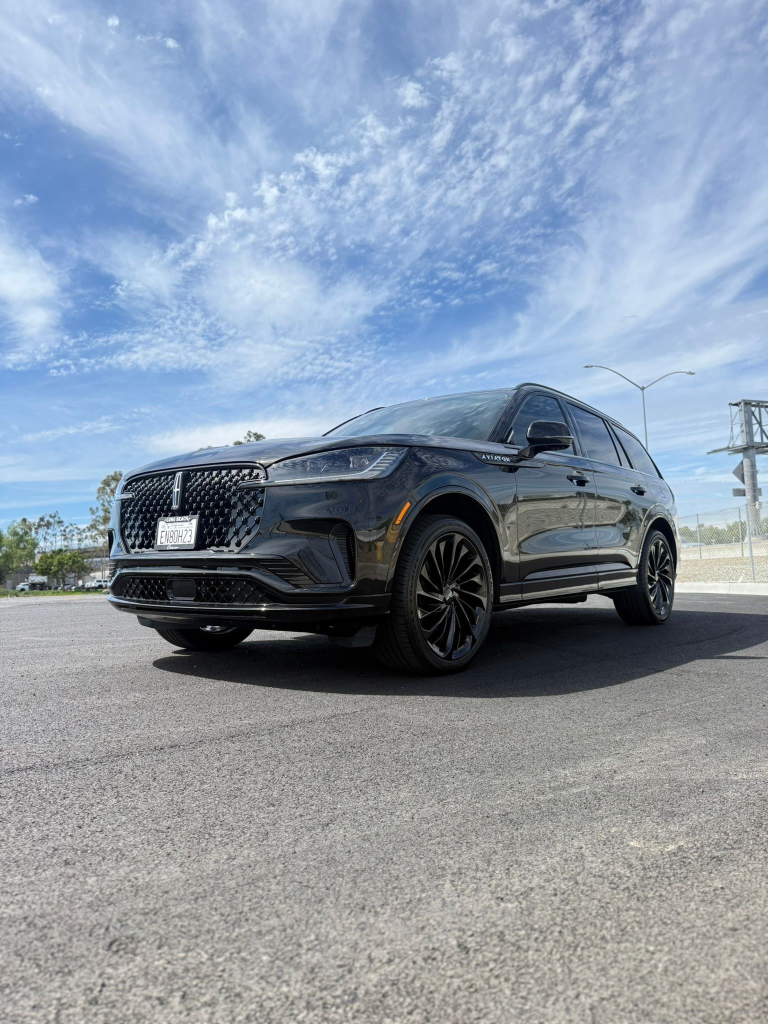 Black sports sedan parked on a sunny road under a partly cloudy sky