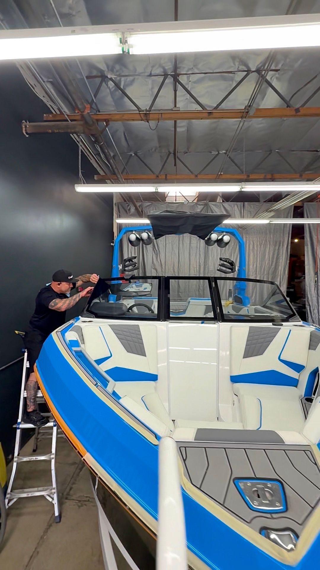 Boat in a workshop, with a worker adjusting the windshield on a white and blue speedboat.