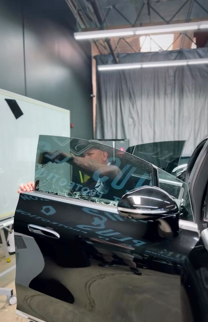Black car with a damaged windshield in a garage, showing reflections and a white wall in the background