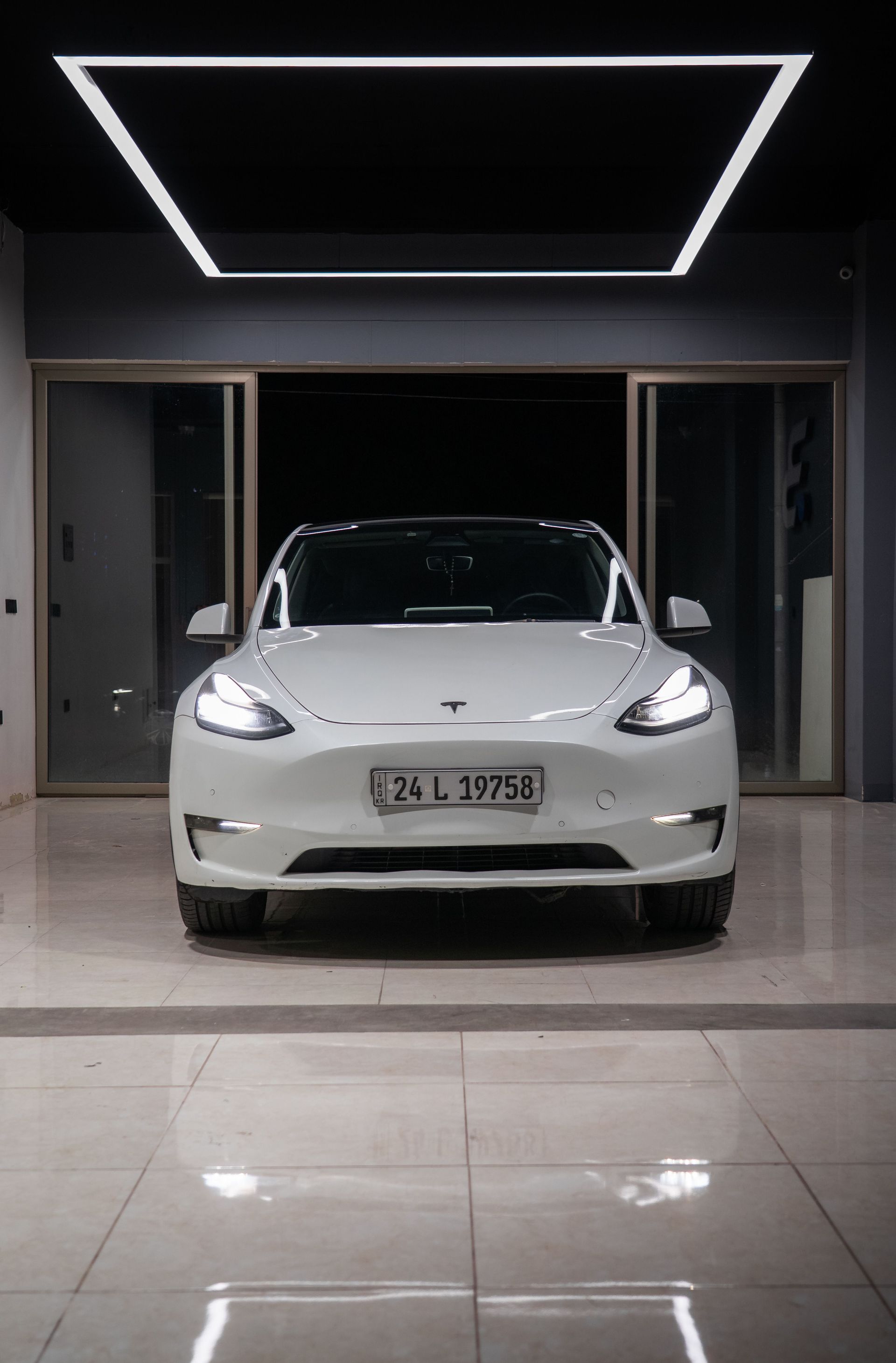White car parked in a modern garage entrance under geometric ceiling lights.