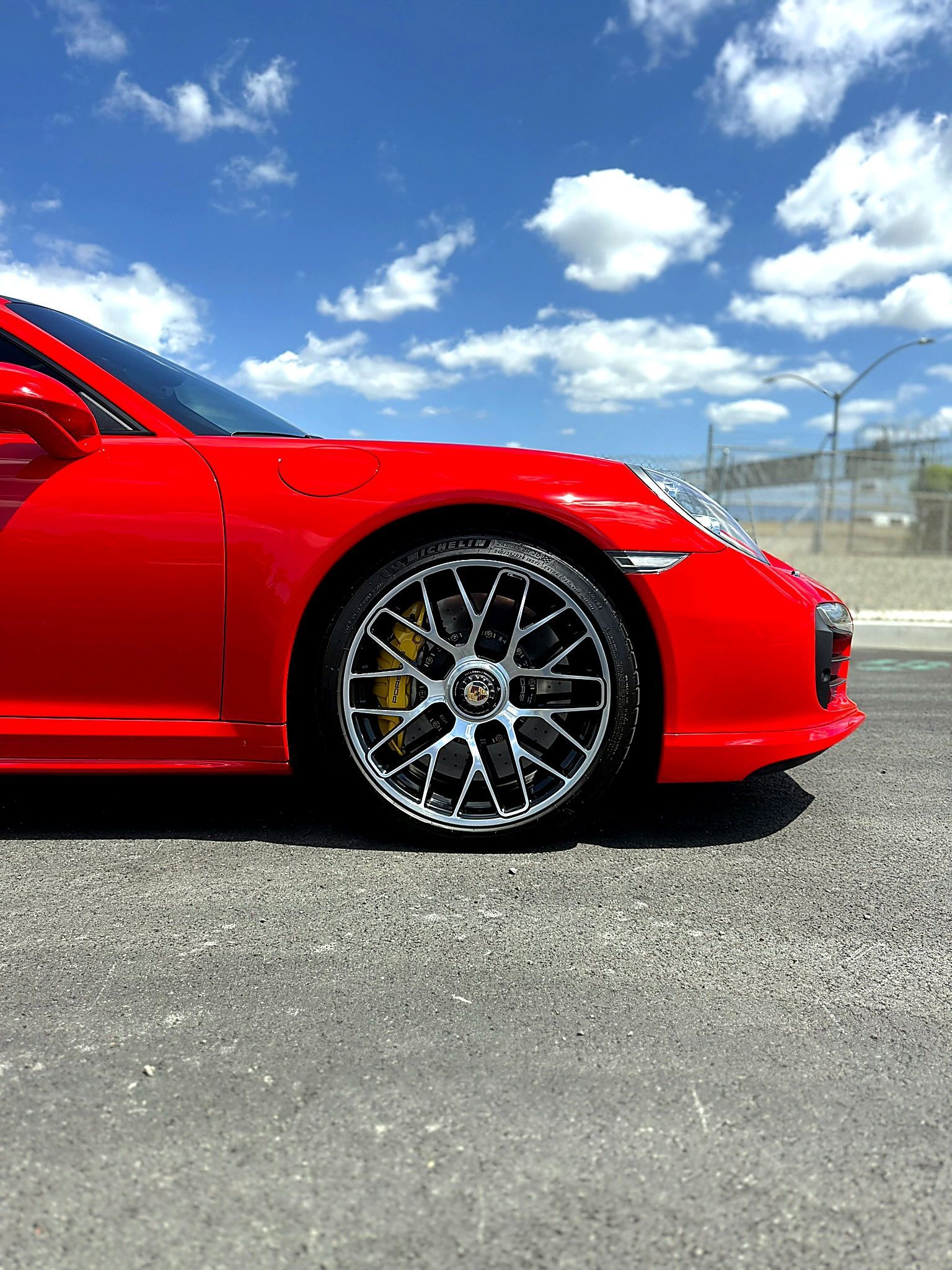 Red sports car parked on asphalt under a bright blue sky, side view showing front wheel.
