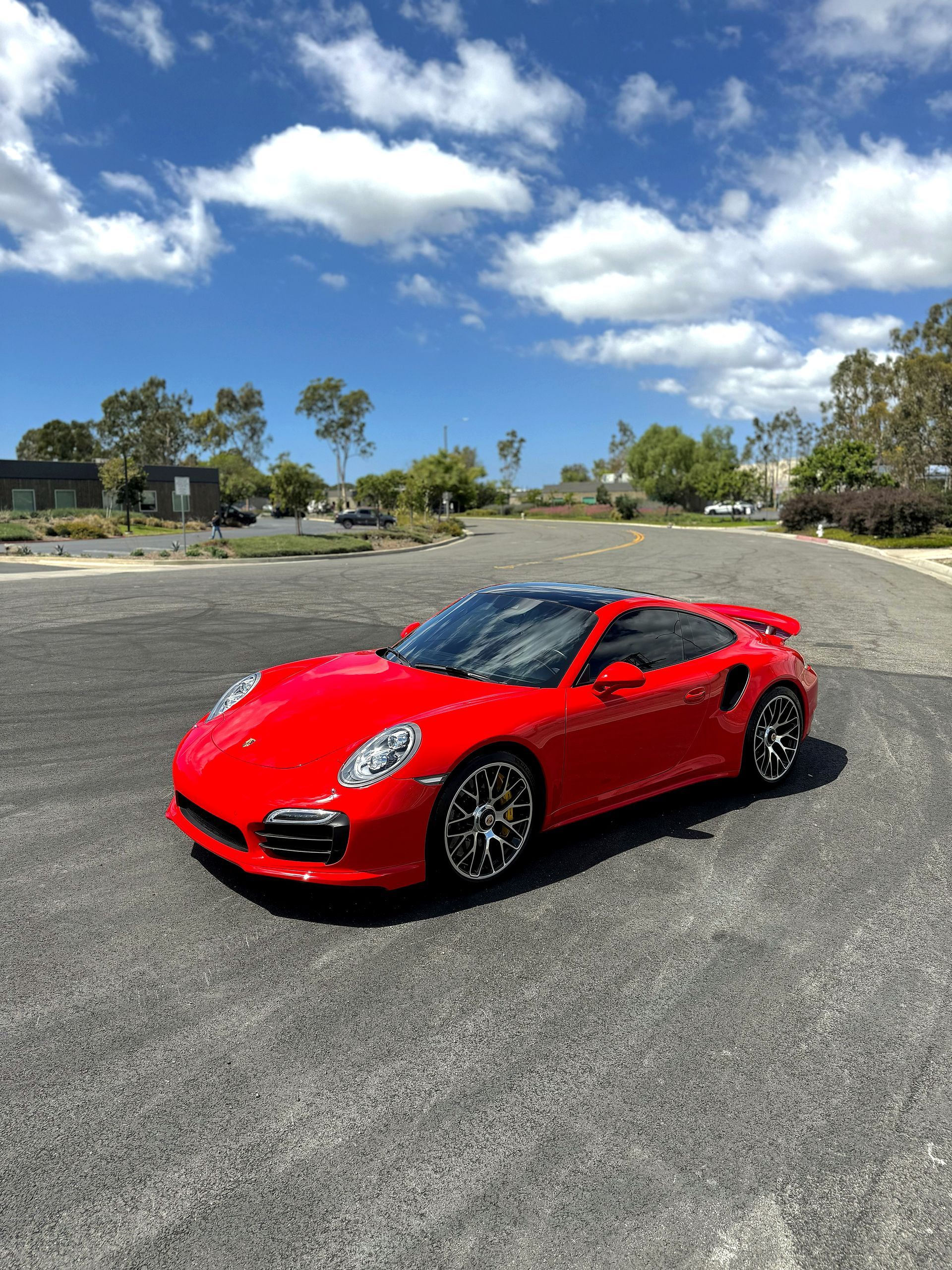 Red sports car parked on an empty asphalt lot under a bright blue sky