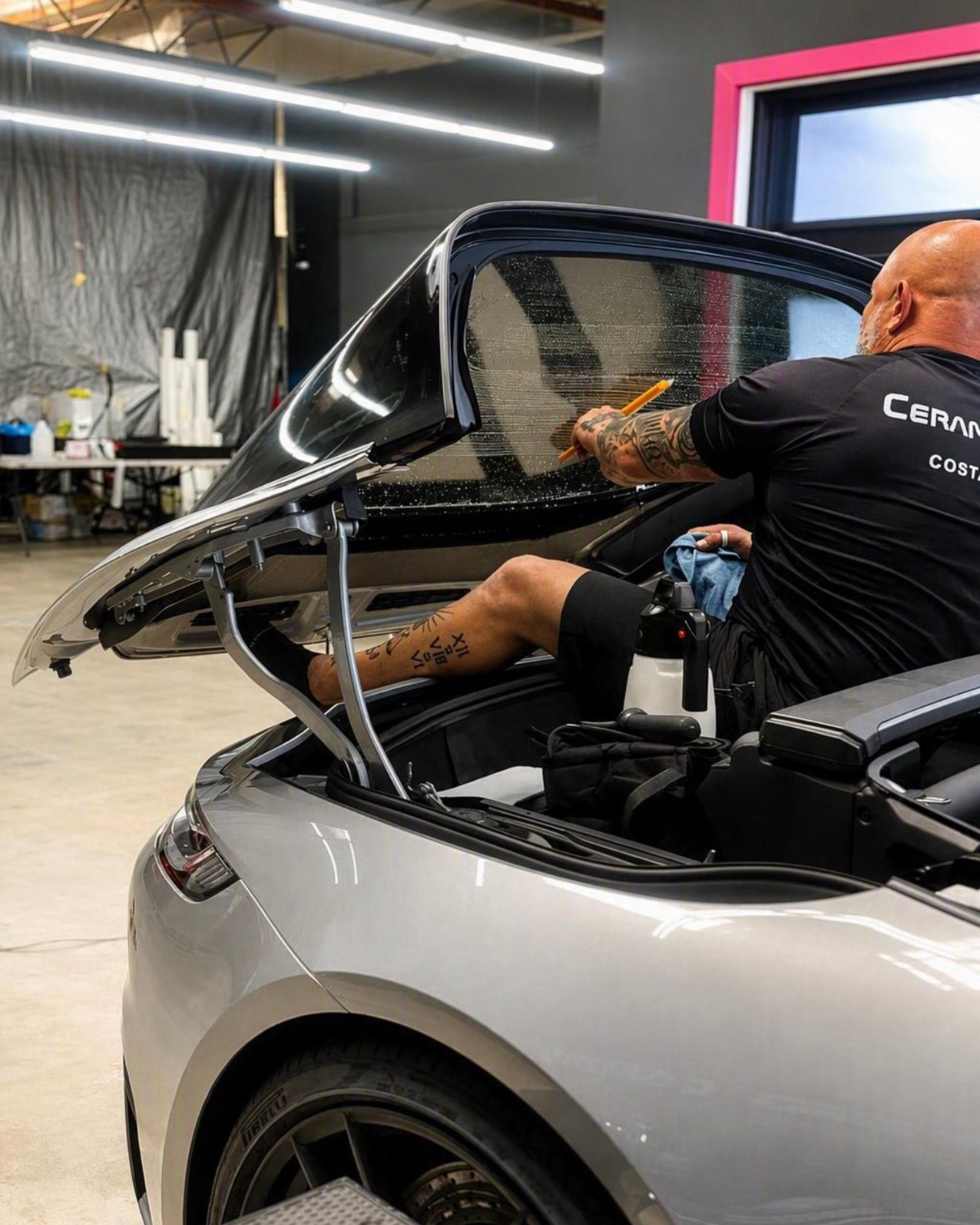 Person working inside a silver convertible with the roof open in a garage