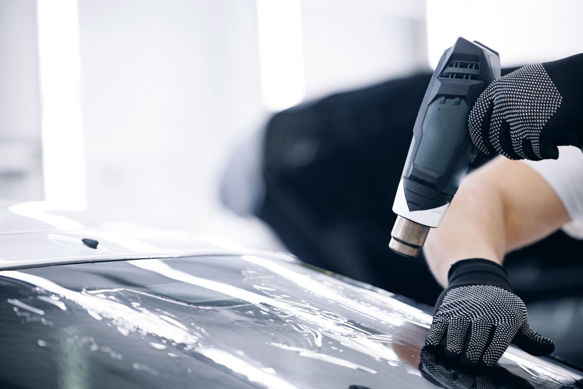 Person using a heat gun to remove film from a car windshield
