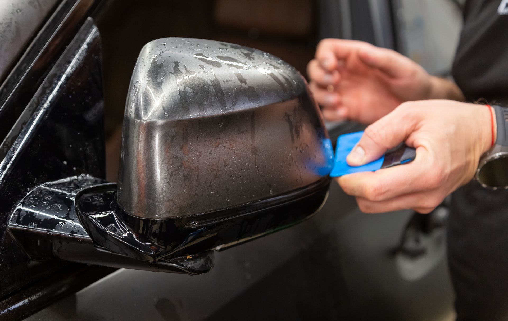 Person cleaning a black car side mirror with a blue cloth