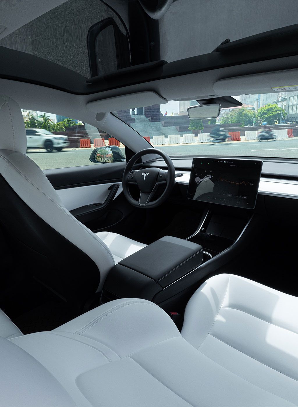 Modern car interior with white seats, black dashboard, and steering wheel, viewed from the back seat