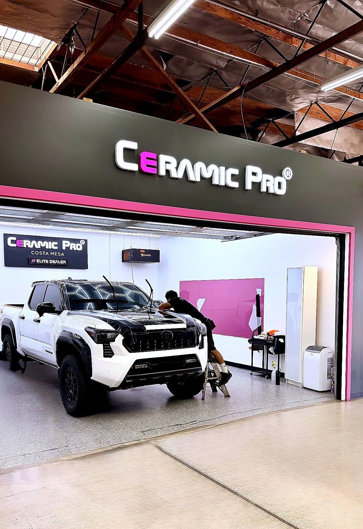 Ceramic Pro storefront with a white off-road truck displayed inside and a dog at the entrance