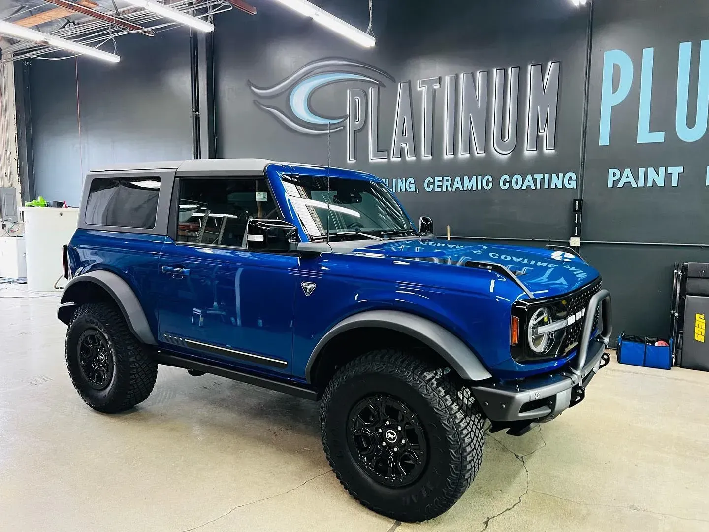 Blue off-road SUV in a garage with a Platinum Plu logo on the wall
