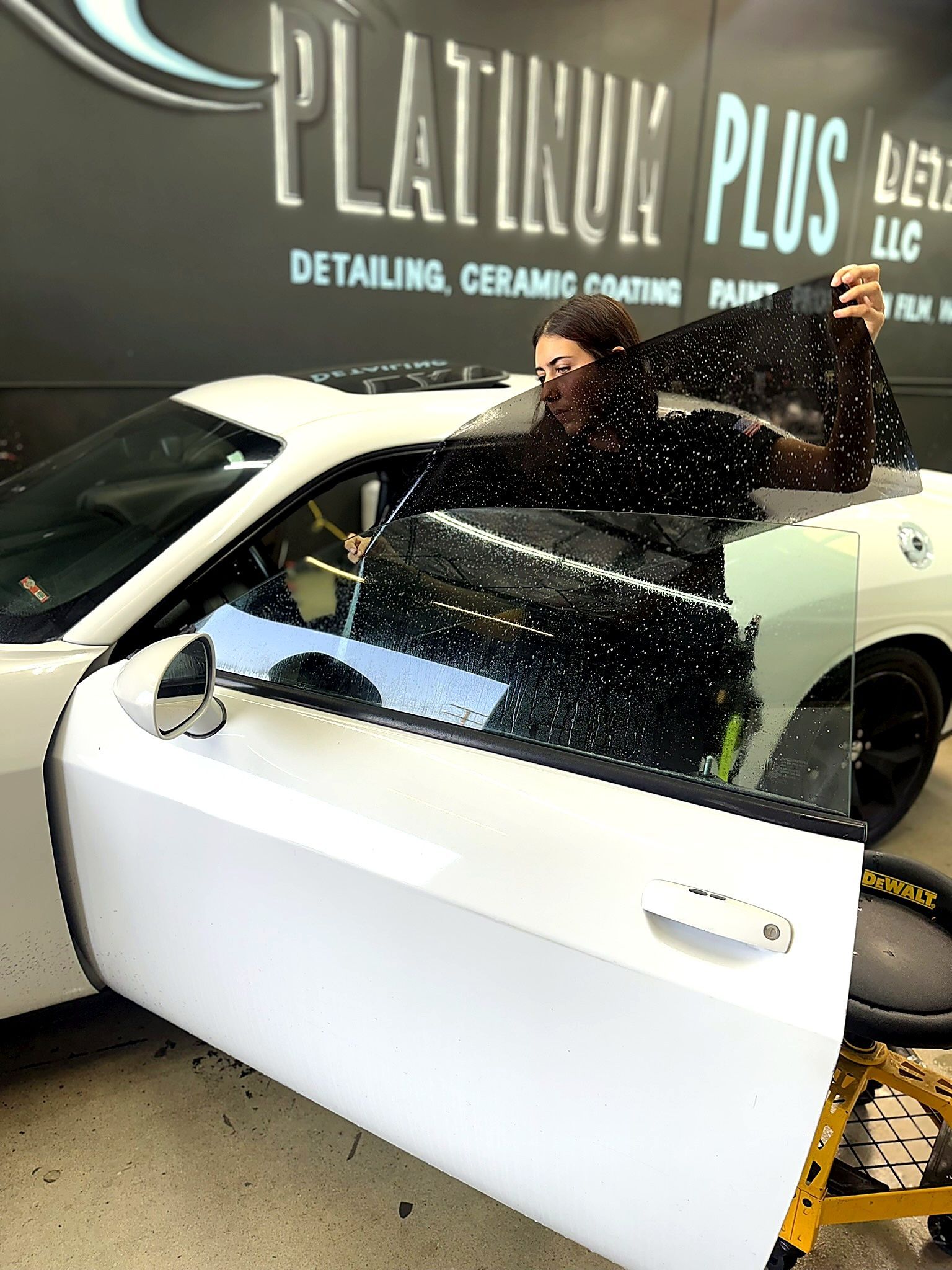 White car hood being polished in a detailing shop with “PLATINUM PLUS” sign in the background